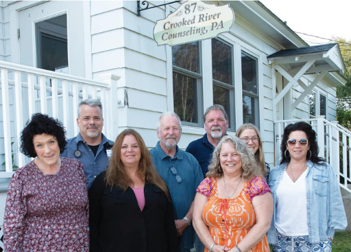 Eight staff members stand in front of a white building with a Crooked River Counseling sign.