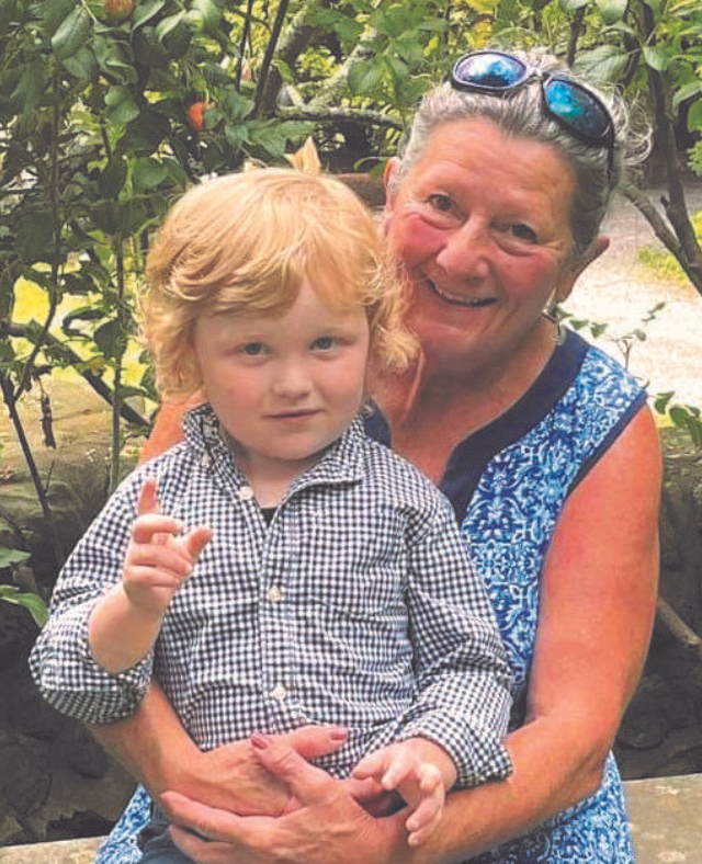 An older woman in a blue dress smiles while hugging a young child with curly blond hair, both enjoying the outdoors in a green garden setting, embodying the warmth and connection celebrated by Maine Voices of Recovery.