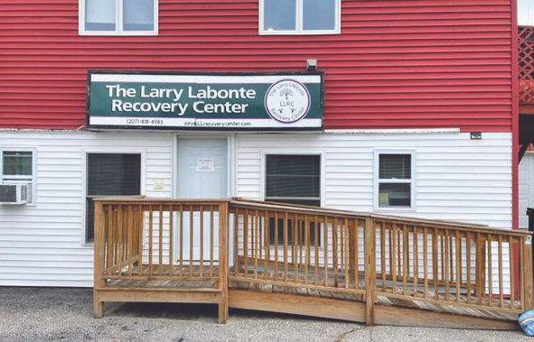 A red and white building with a wooden wheelchair ramp leads to the door, where a sign above warmly welcomes visitors to the Larry Labonte Recovery Center.
