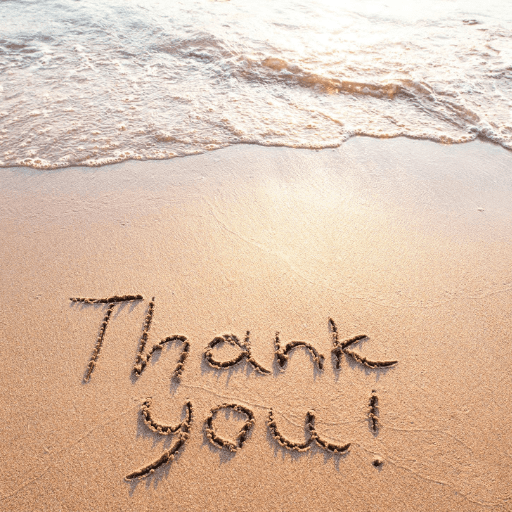Thank you! is written in the sand on a beach near the shoreline, with gentle waves approaching in the background, capturing a moment of gratitude and mindfulness.