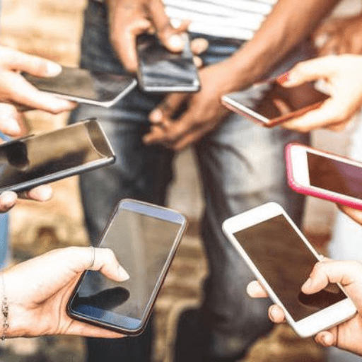 Several people with smartphones form a circle, focusing intently on their devices—a scene that highlights the growing impact of NoMoPhobia. Hands and phones are clear, while faces remain mostly out of frame or blurred.