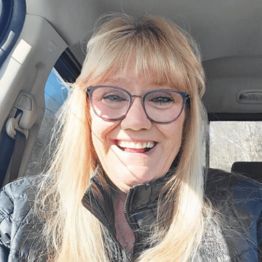 A woman with long blonde hair and glasses smiles brightly while sitting in a car, sunlight on her face—a moment that captures the essence of Stories Restoring Hope.