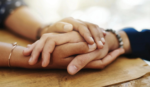 Multiple hands stacked together on a wooden surface, showing support and unity among a group.