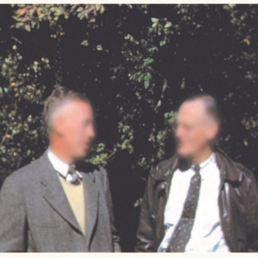 Two men stand outdoors in front of leafy trees, faces blurred. One wears a suit and tie with a sweater, the other a leather jacket over a shirt and tie—possibly attending an Alcoholics Anonymous Service Committees event.