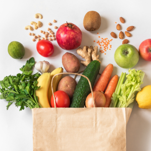 Paper grocery bag overflowing with fresh fruits, vegetables, nuts, and ginger arranged on white background.