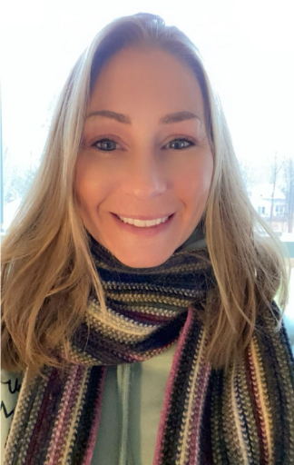 Woman with long blonde hair wearing striped scarf smiles at camera indoors.