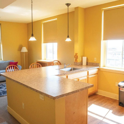 Bright yellow kitchen with island countertop, pendant lights, sink, and large windows overlooking a city.