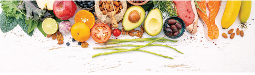 Colorful fresh produce and prepared foods arranged on white surface, including fruits, vegetables, nuts, and bread.
