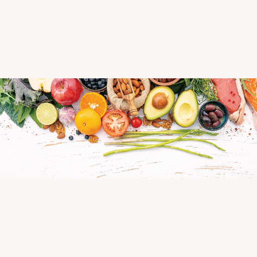 Assorted fresh fruits, vegetables, and proteins arranged on a white wooden surface, including avocado, tomatoes, berries, citrus, and nuts.