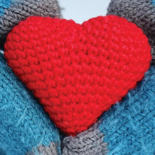 Hands in blue and gray knitted gloves hold a red knitted heart shape.