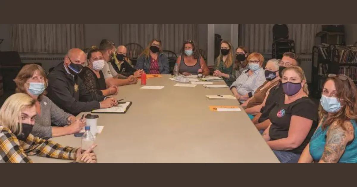 A large group of people seated around a long conference table, wearing face masks.