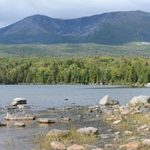 Mount Katahdin rising above a forested shoreline and a boulder-strewn lake.