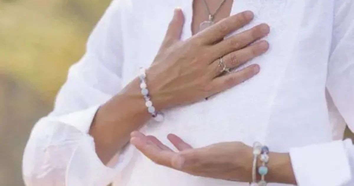 Close-up of a person's hands crossed over their chest, wearing white linen and beaded bracelets.
