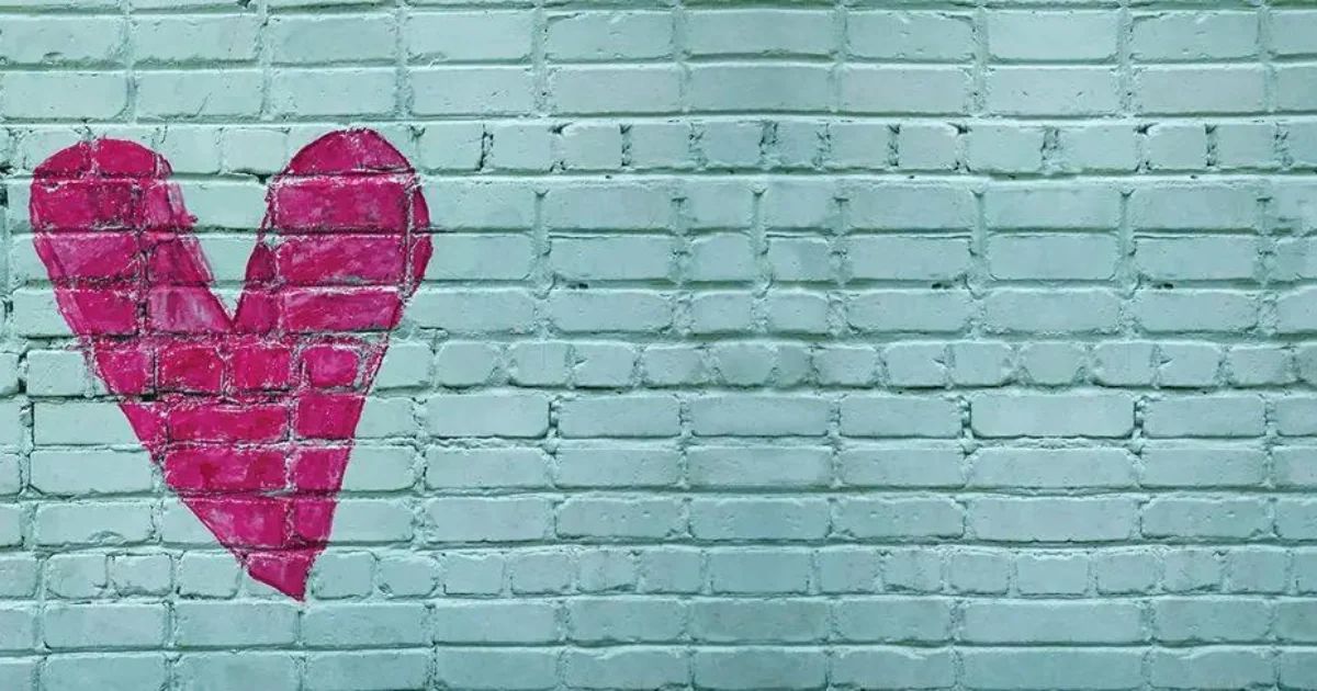 A pink heart painted on a pale turquoise brick wall.