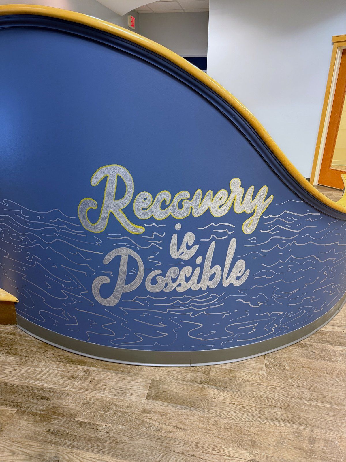 A curved blue wall with the words “Recovery is Possible” painted in script.