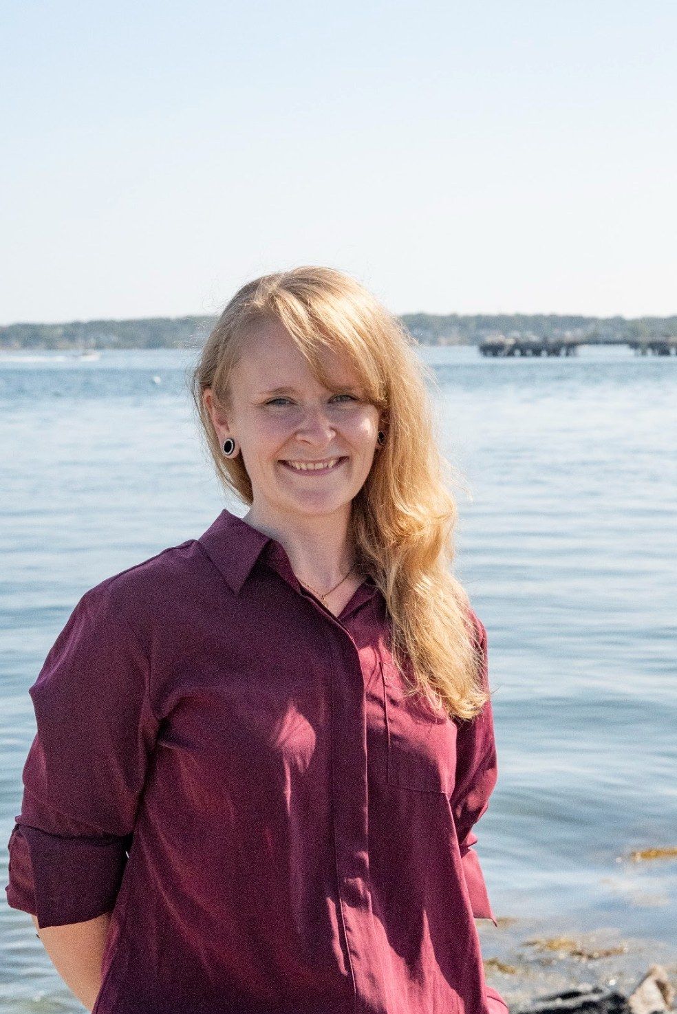 Ali, smiling, standing at the water’s edge in a maroon shirt.