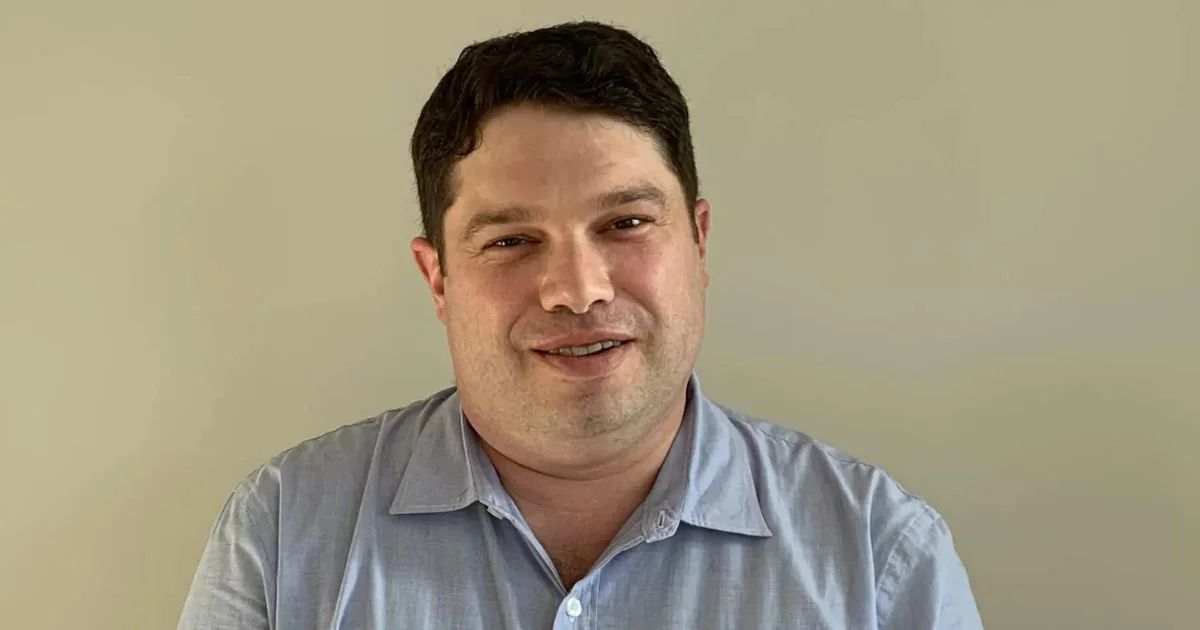 Portrait of a man in a light blue shirt against a plain wall.