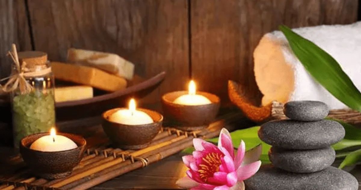 A spa arrangement of lit candles, smooth stones, a pink lotus flower and rolled towels.