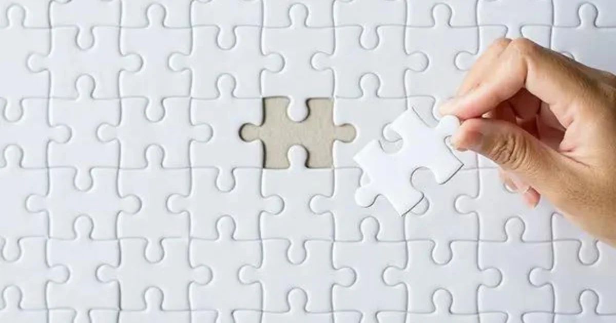 A hand placing the final piece into an otherwise complete white jigsaw puzzle.