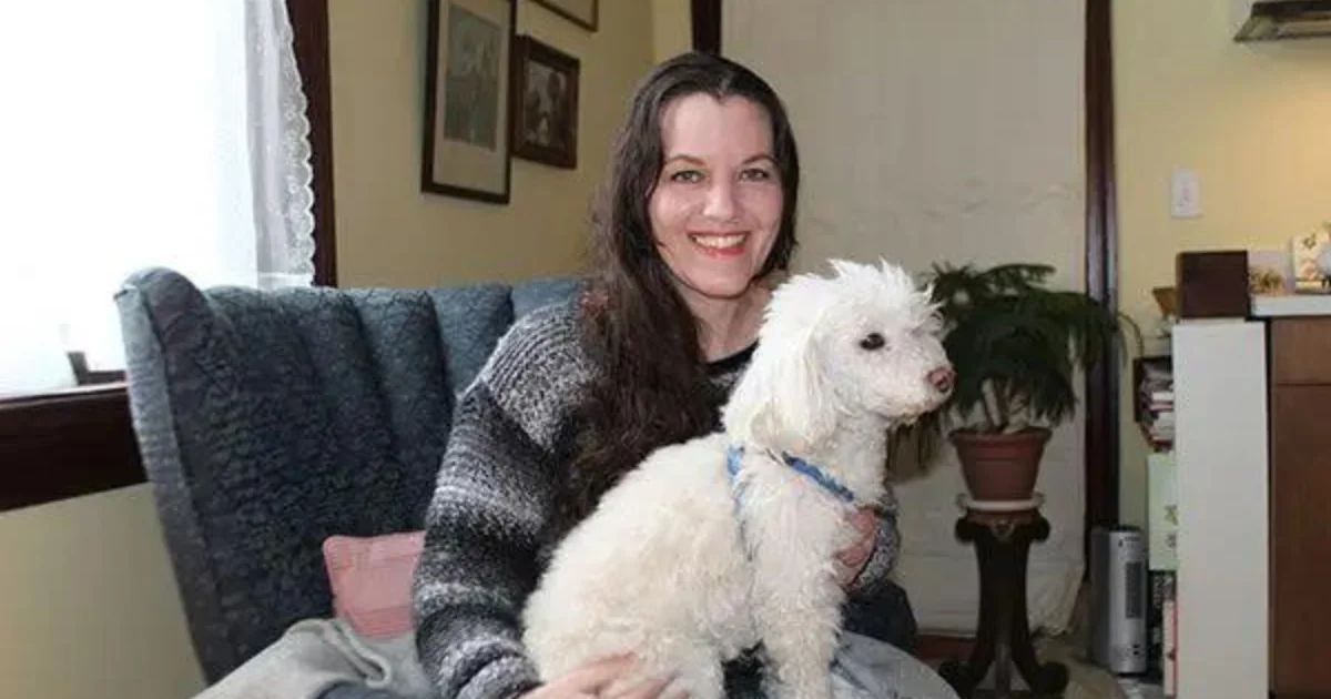 Tricia Grant seated in an armchair holding a small white dog.