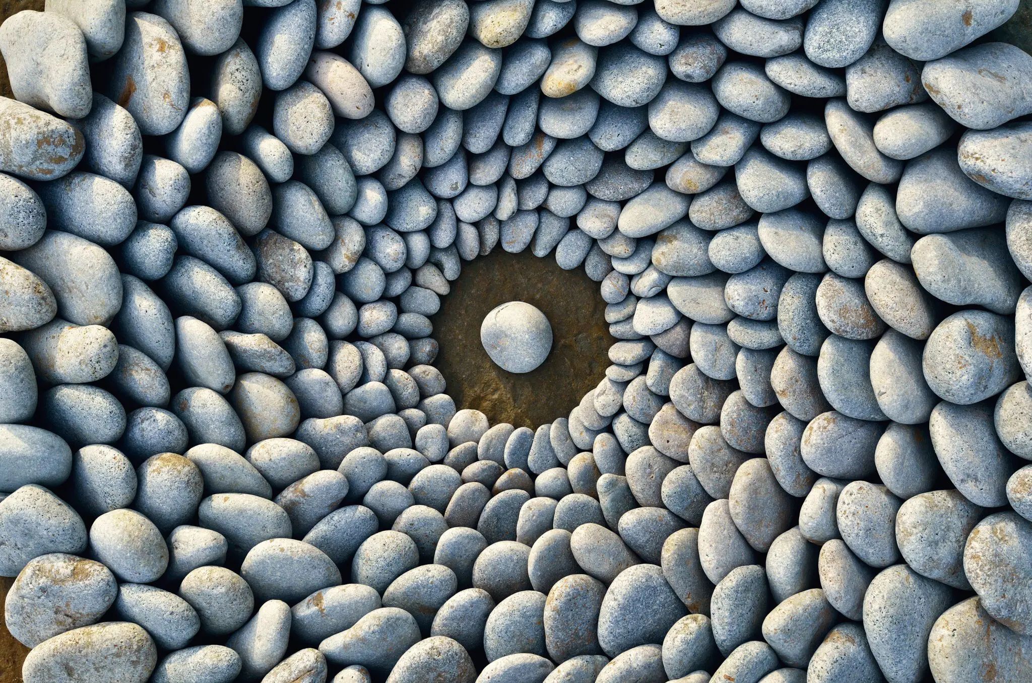 Smooth river stones arranged in concentric circles with one centered stone in a dark pool.