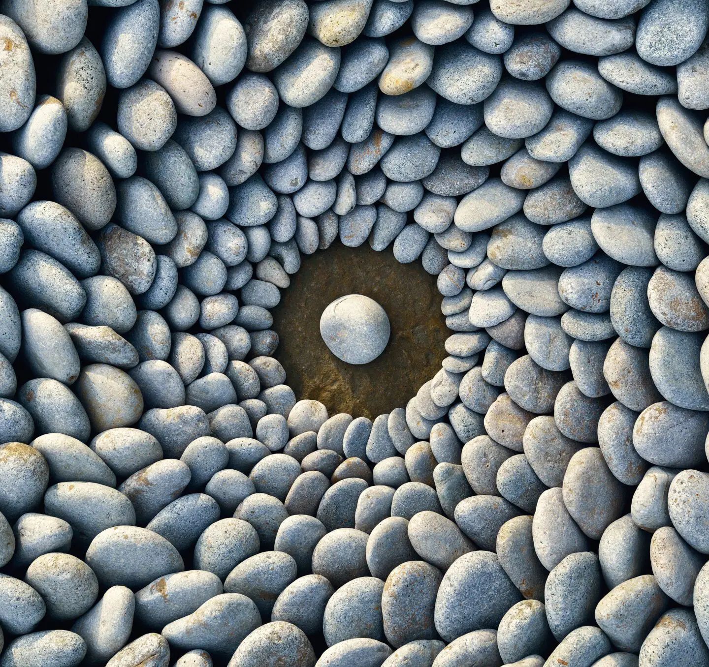 Smooth river stones arranged in concentric circles with one centered stone in a dark pool.