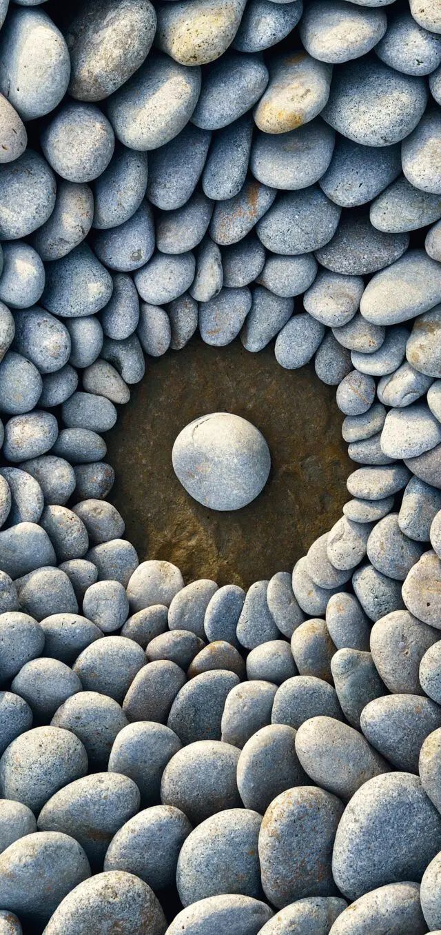 Smooth river stones arranged in concentric circles with one centered stone in a dark pool.