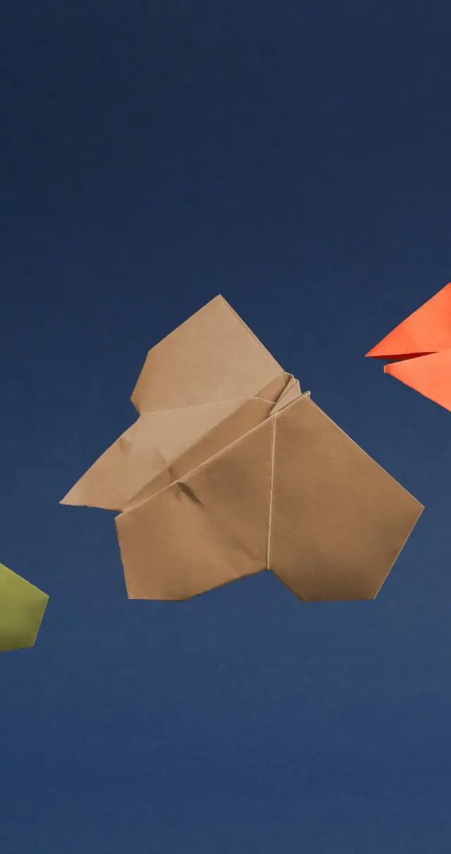 Origami paper shapes in green, yellow, tan, and orange arranged on a dark blue background in increasing sizes.