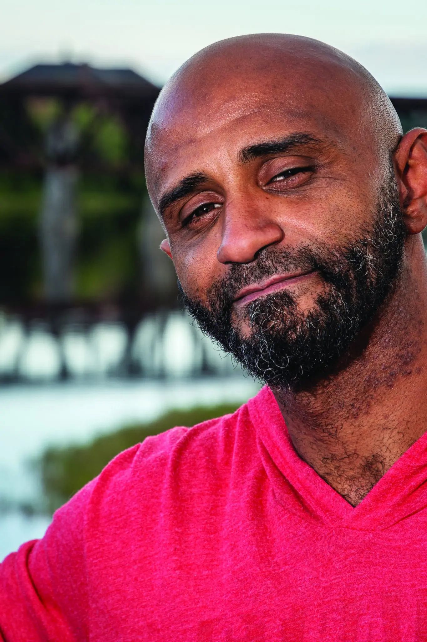 Marshall Mercer, a man with a beard wearing a bright pink shirt, smiles outdoors with a blurred building behind him.