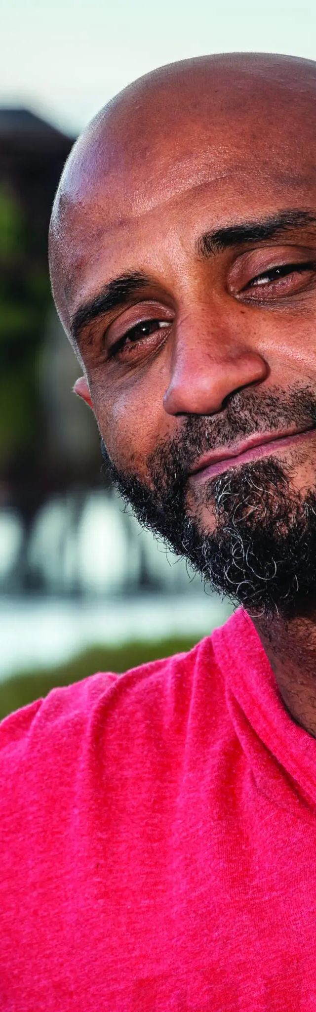 Marshall Mercer, a man with a beard wearing a bright pink shirt, smiles outdoors with a blurred building behind him.